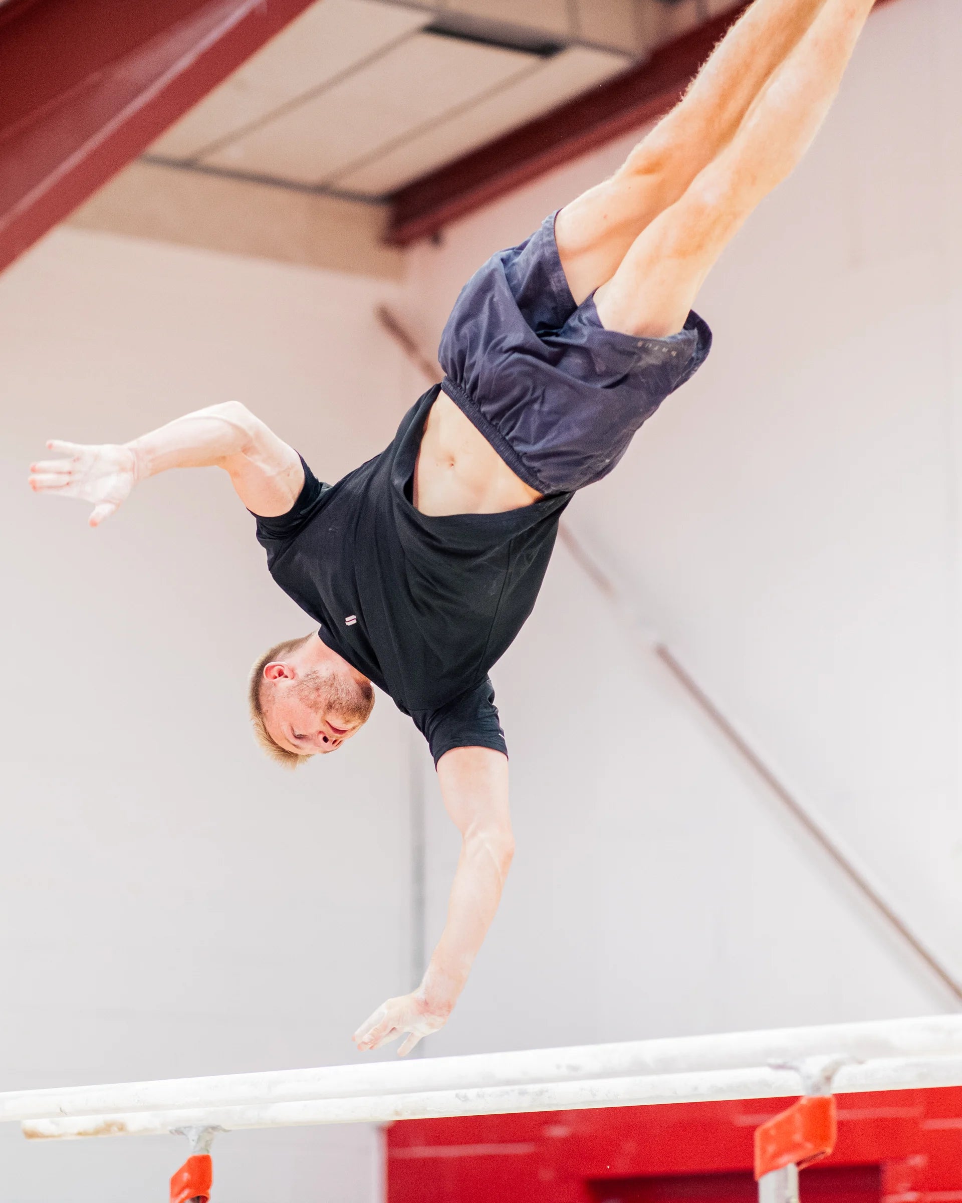 Person performing a gymnastics skill on the parallel bars wearing sports t-shirt and training shorts.