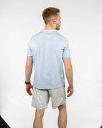 Man wearing a light blue t-shirt that says "satus" down the middle, and tan shorts on a white background