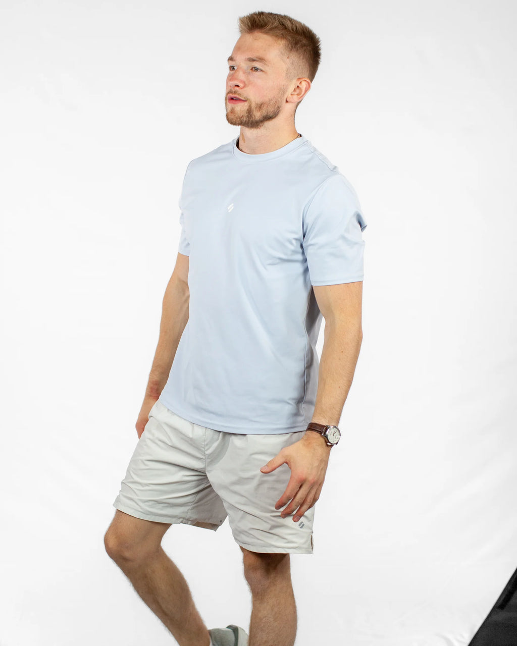 Man wearing a light blue t-shirt and beige shorts on a white background