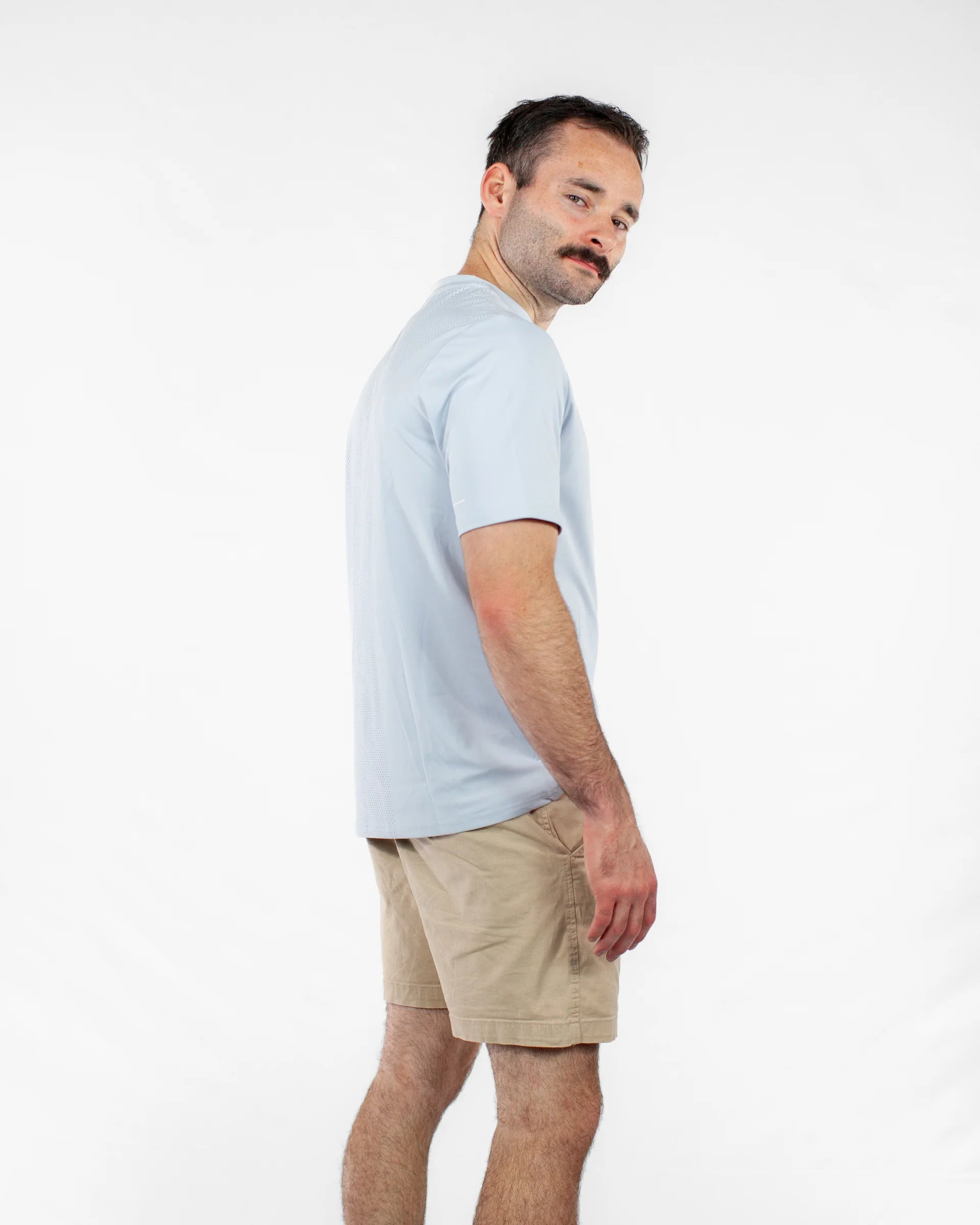 Man wearing a light blue t-shirt and beige shorts on a white background