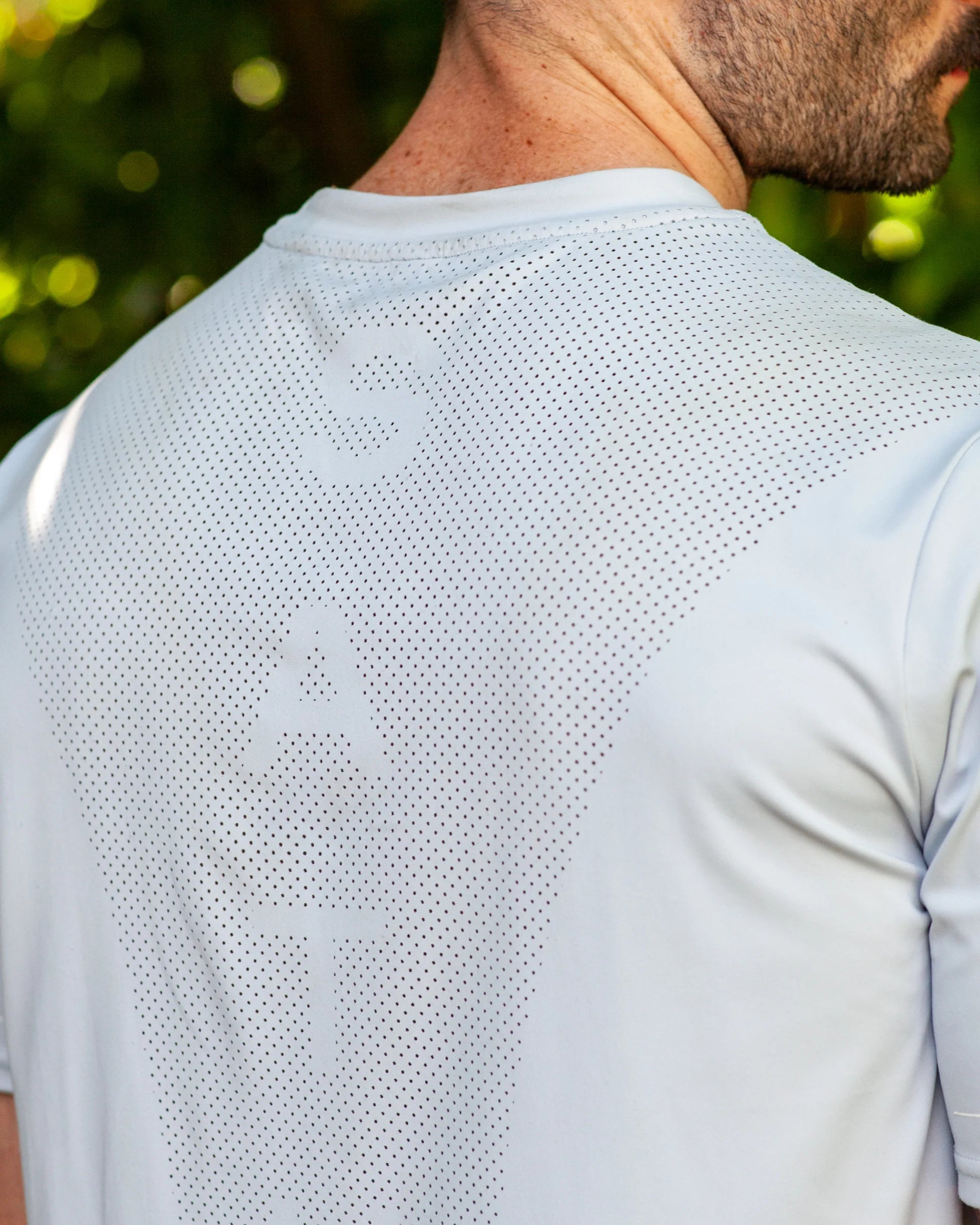 Blue athletic shirt with perforated design on the back, worn by a person outdoors.