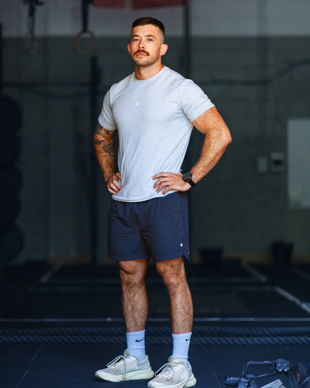 Man in athletic blue t-shirt and grey training shorts standing in a gym setting