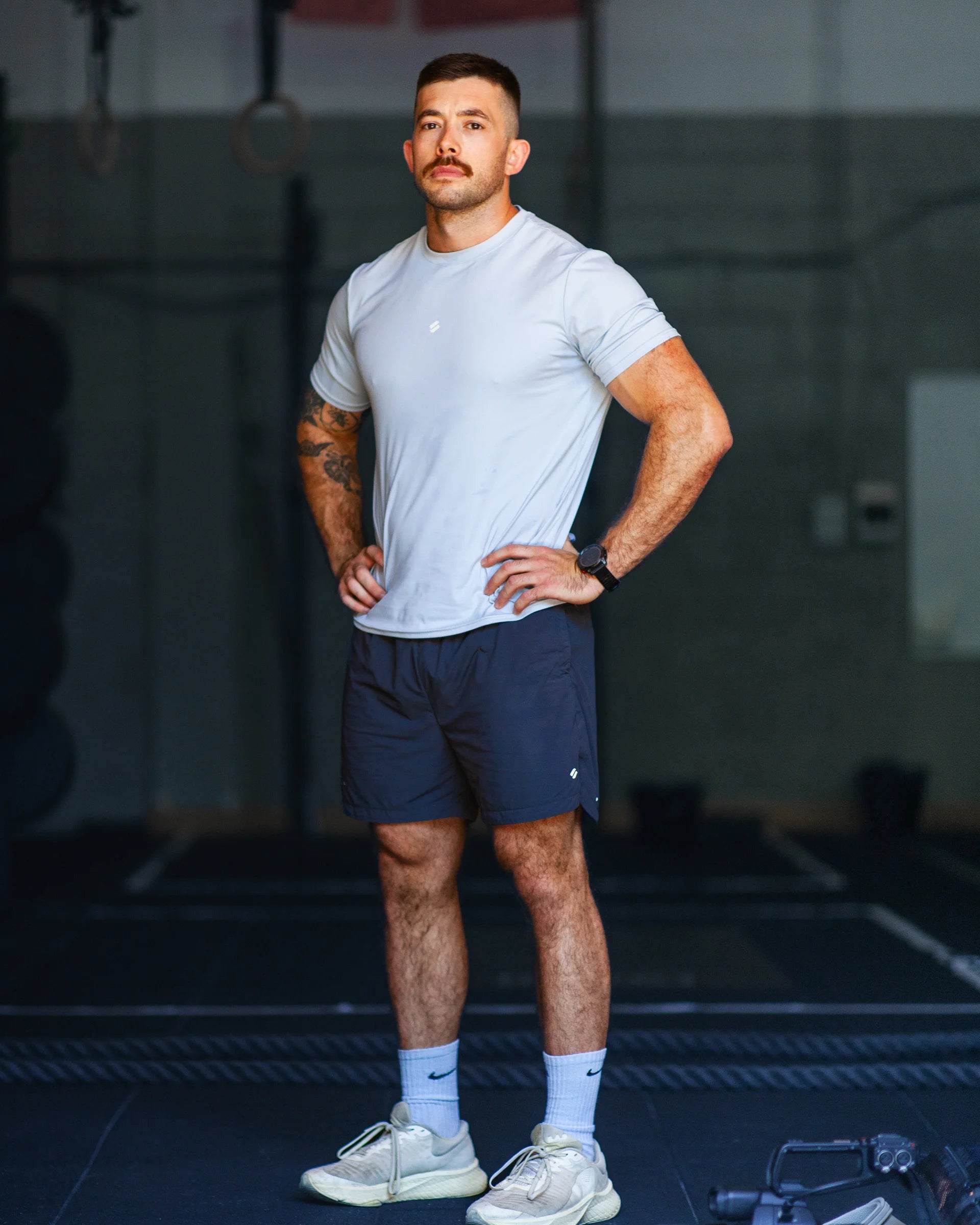Man in athletic blue t-shirt and grey training shorts standing in a gym setting