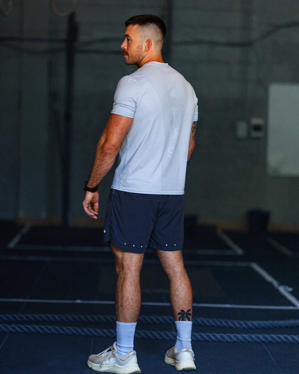 Man wearing a blue t-shirt and dark grey shorts in a workout gym.