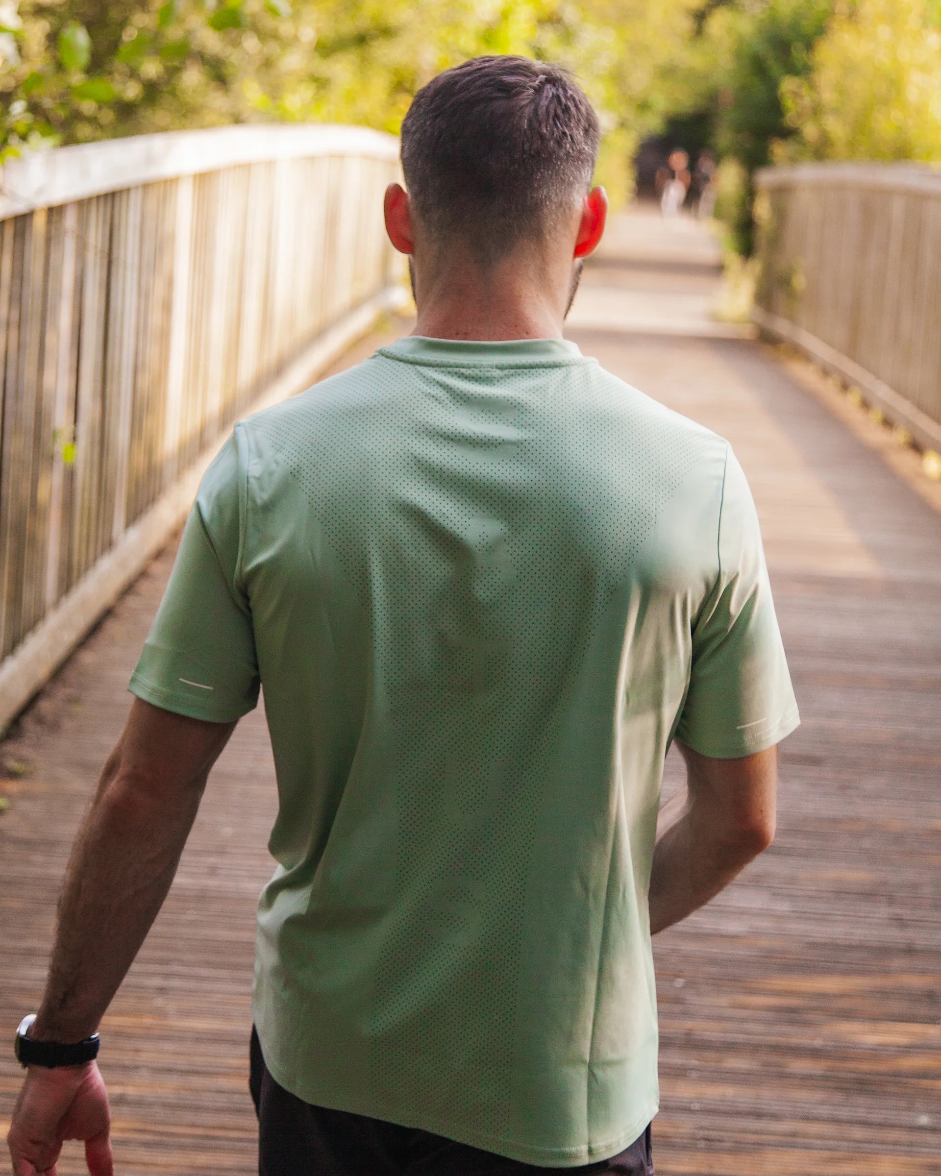 Man in a green sports shirt walking on a wooden path with trees in the background