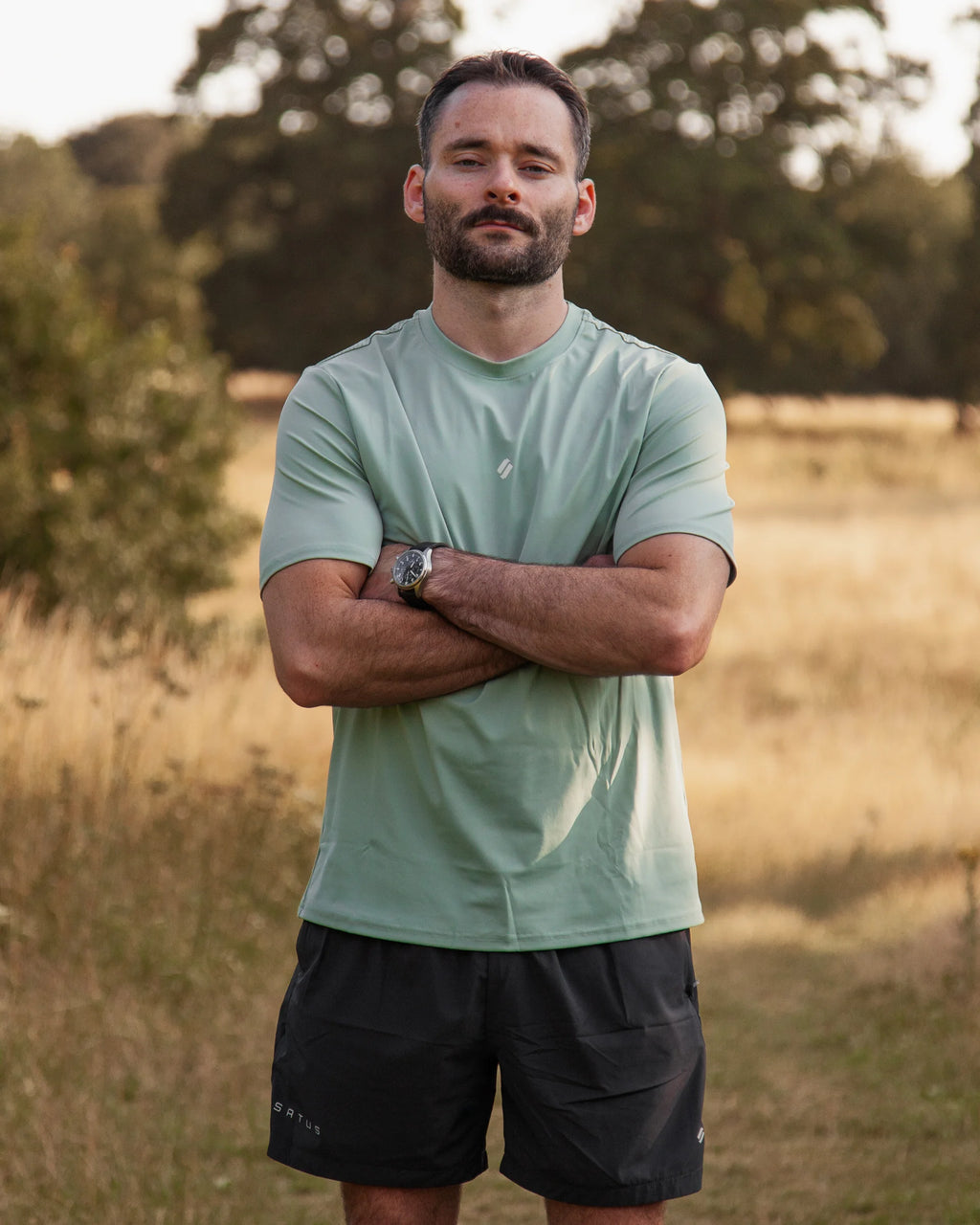 Man standing in a field wearing a light green t-shirt and black training shorts.