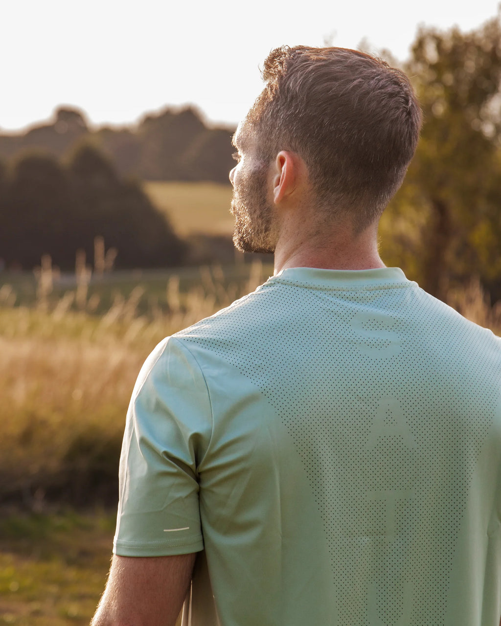 Man wearing a green sports shirt standing in a field with trees in the background