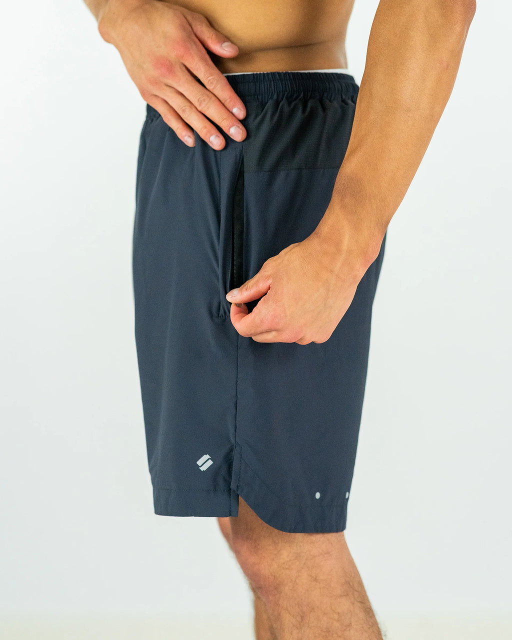Person using zip on dark grey shorts worn by a person on a white background